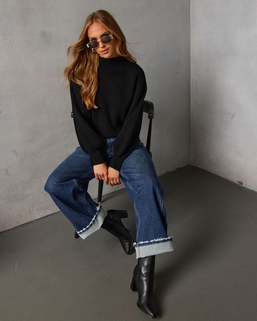 Black mock neck knit sweater with long sleeves, styled with cuffed jeans and boots.