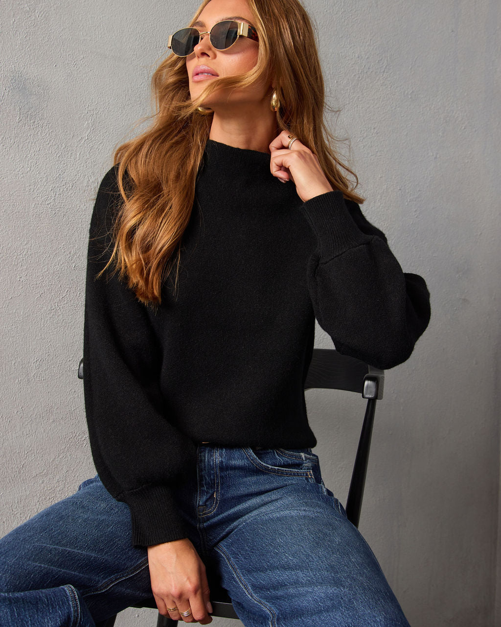 Black mock neck sweater with high neckline and long cuffed sleeves, paired with jeans.