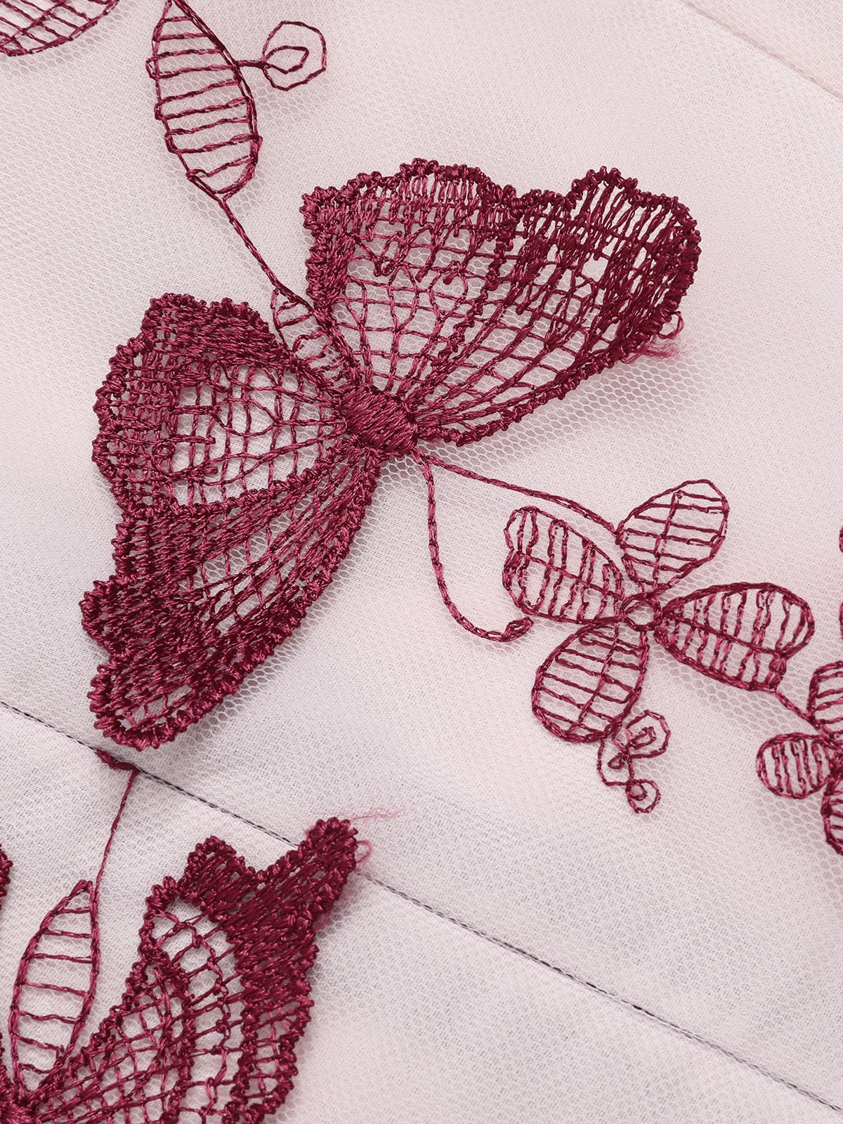 Close-up of butterfly embroidery on sheer fabric, stitched details in wine red on light base