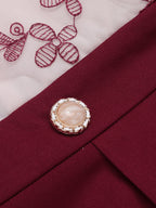 Close-up of round faux pearl button on wine red jumpsuit waist, with butterfly embroidery