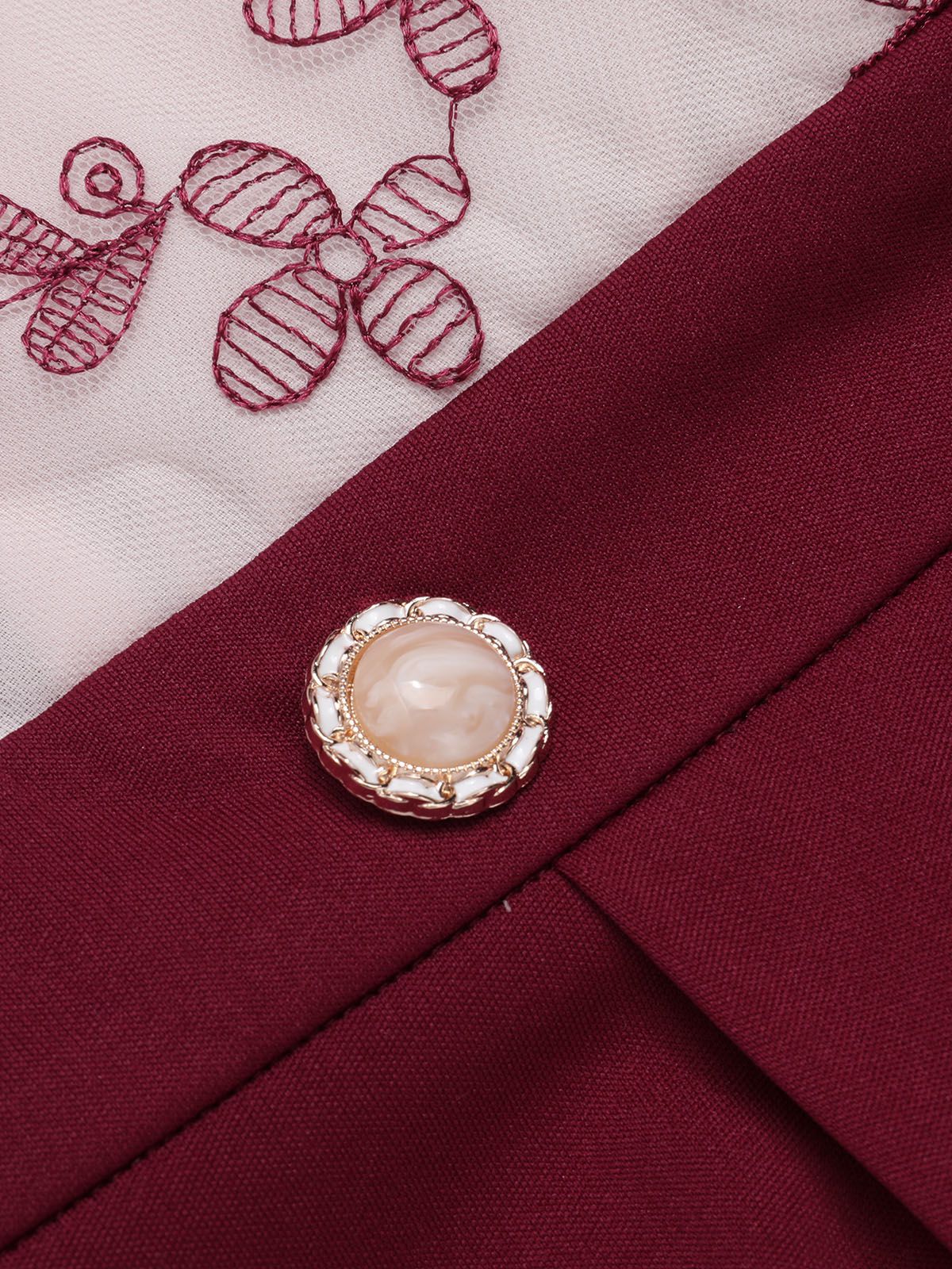 Close-up of round faux pearl button on wine red jumpsuit waist, with butterfly embroidery