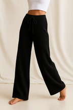 Black high-waisted wide-leg lounge pants with drawstring, worn with bare feet.