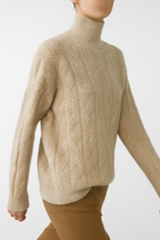 Beige cable knit mock neck sweater with long sleeves and ribbed neckline, cuffs, hem.