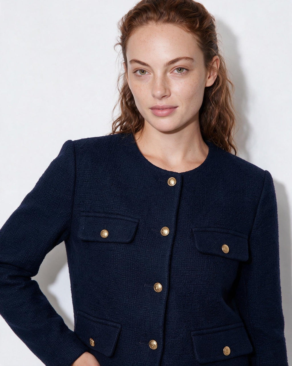 Women’s navy cropped collarless jacket close-up, gold buttons and flap pockets detail.