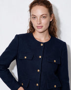 Women’s navy cropped collarless jacket close-up, gold buttons and flap pockets detail.