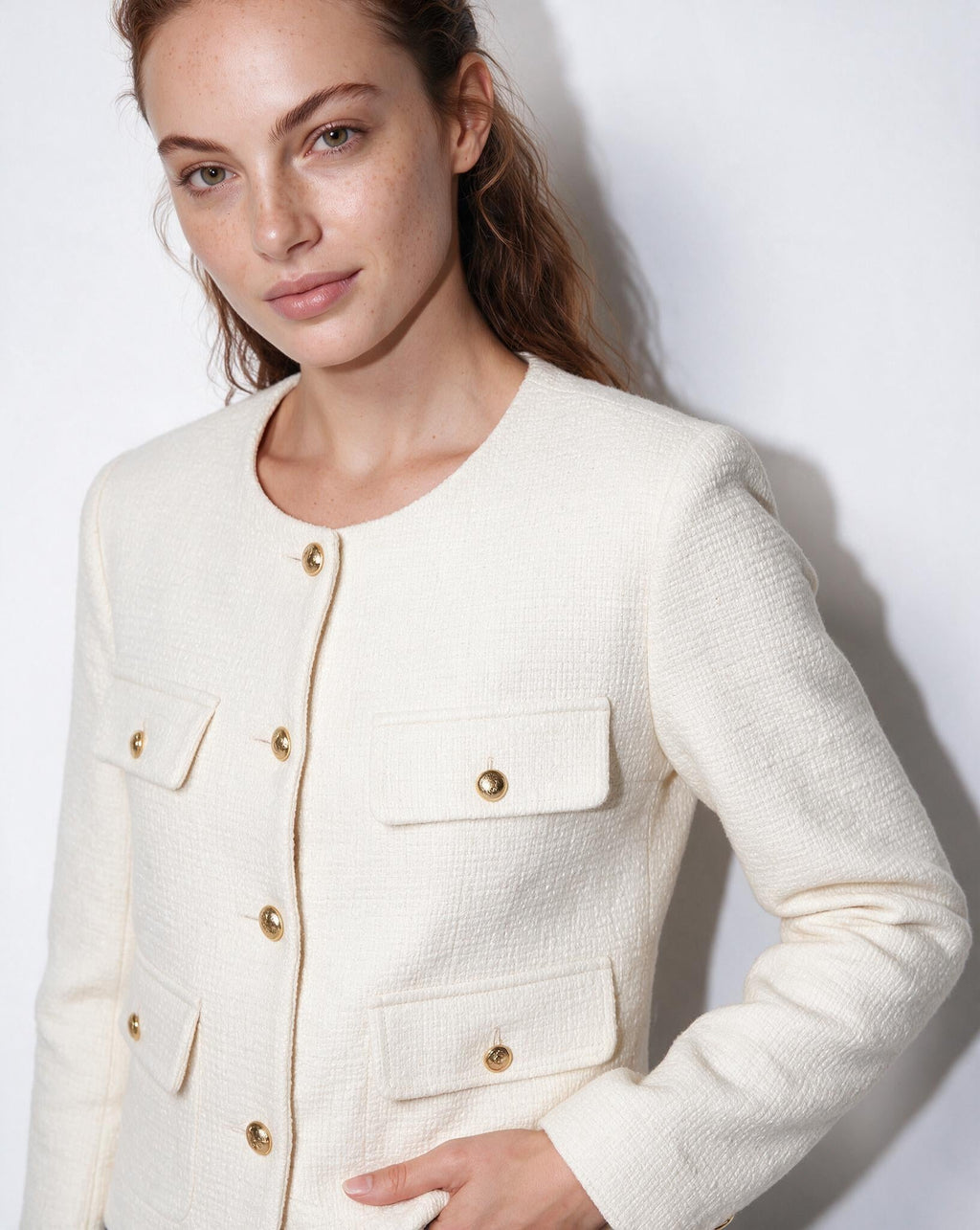 Women’s cream cropped collarless jacket close-up, gold buttons and four flap pockets.