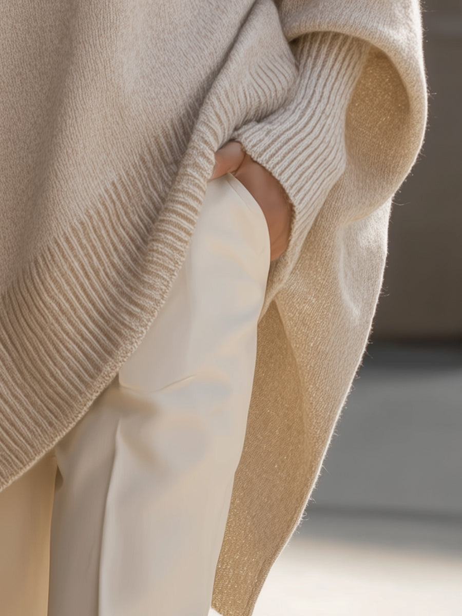 Beige oversized knit sweater draped over white pants; ribbed cuff and hem
