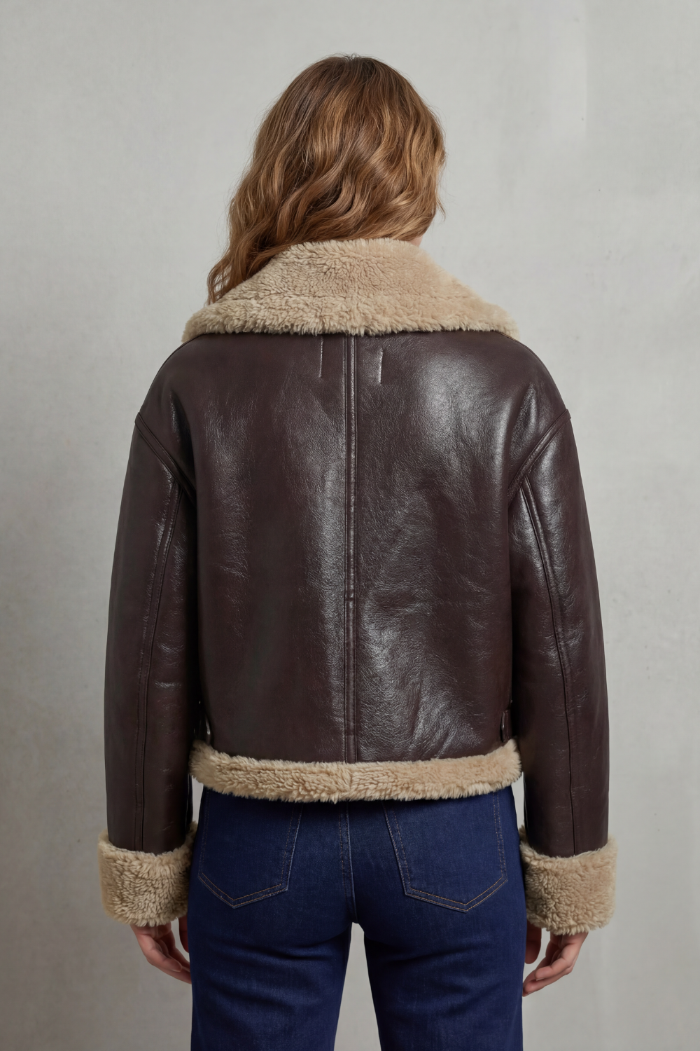 Back view of dark brown cropped aviator jacket with tan fleece hem and cuffs; center zip.