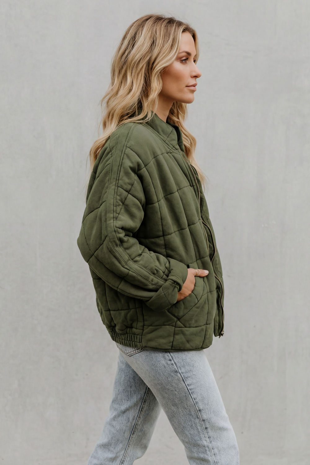 Dark green quilted women’s jacket, side view with full sleeves and front zipper.
