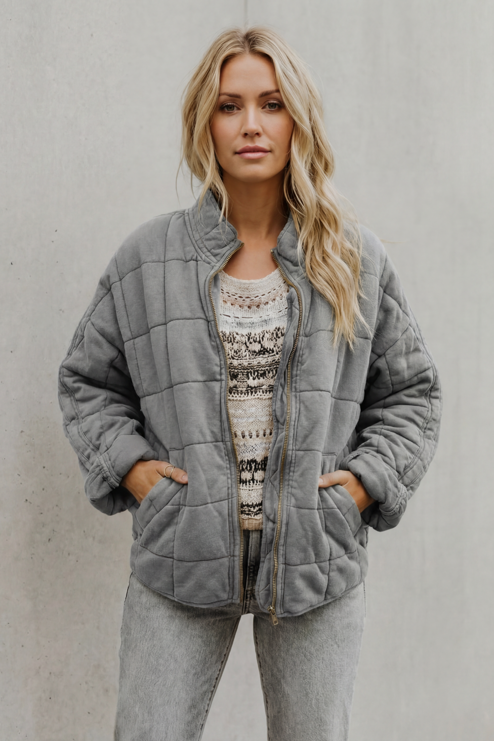 Grey quilted women’s jacket with front zipper, stand collar, and side pockets.