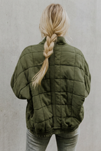 Dark green quilted women’s jacket, back view with quilted panels and elastic hem.