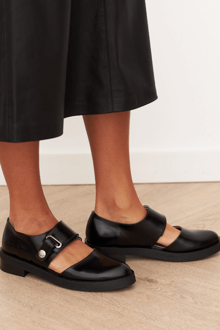 Women's black leather loafers with buckle strap and flat outsole, side view.