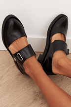 Women's black leather loafers with buckle strap detail, angled toe close-up.