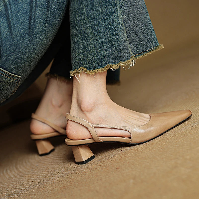 Beige leather slingback heels with pointed toes and low block heels on feet.