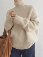 Beige turtleneck knit sweater with ribbed collar and wide long sleeves.