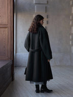 Dark gray long belted wool coat with stand collar, shown from the side