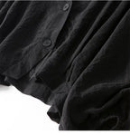Black linen blouse close-up: textured fabric, button placket, draped hem