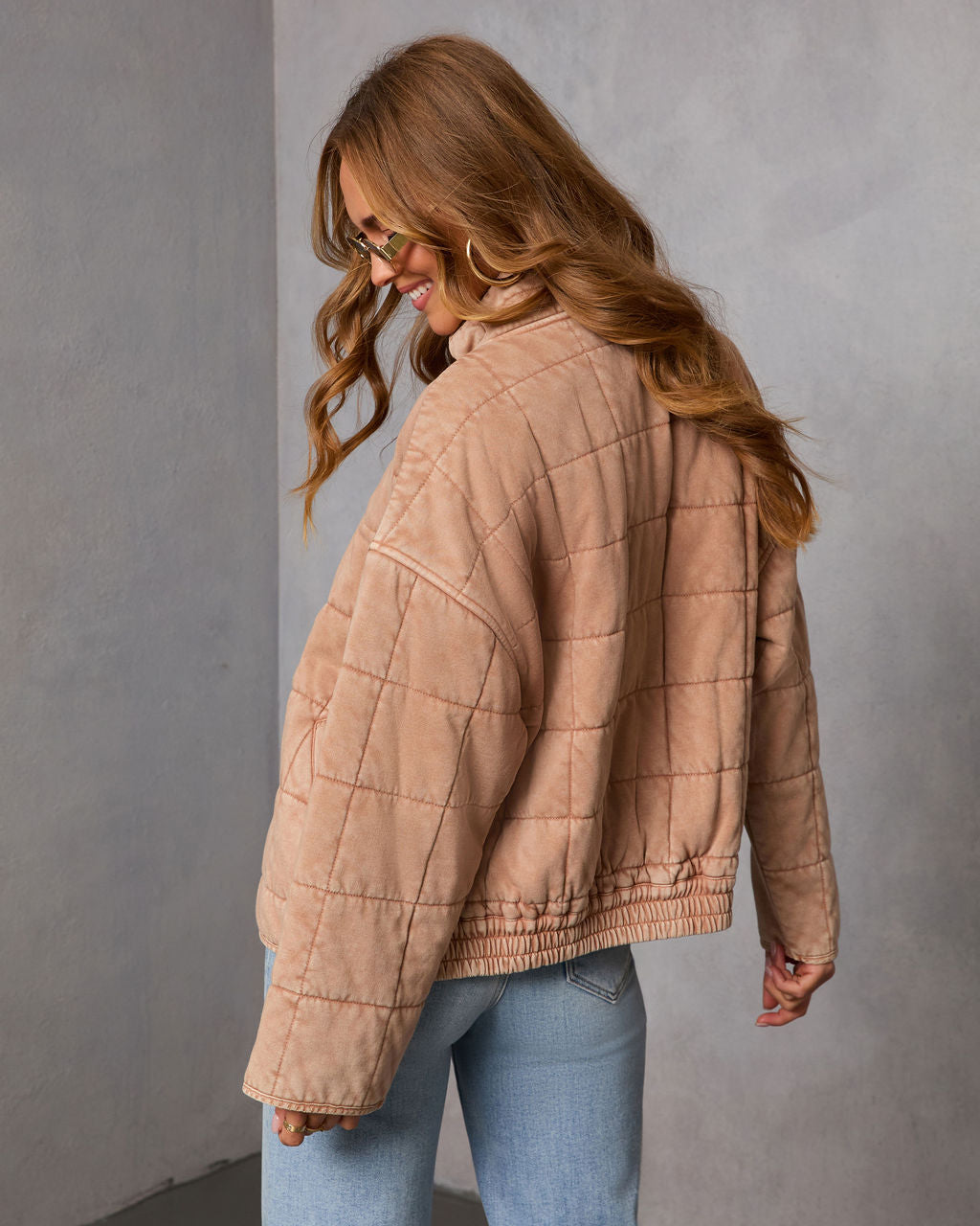 Back view of tan quilted zip jacket with long sleeves and elastic hem detail