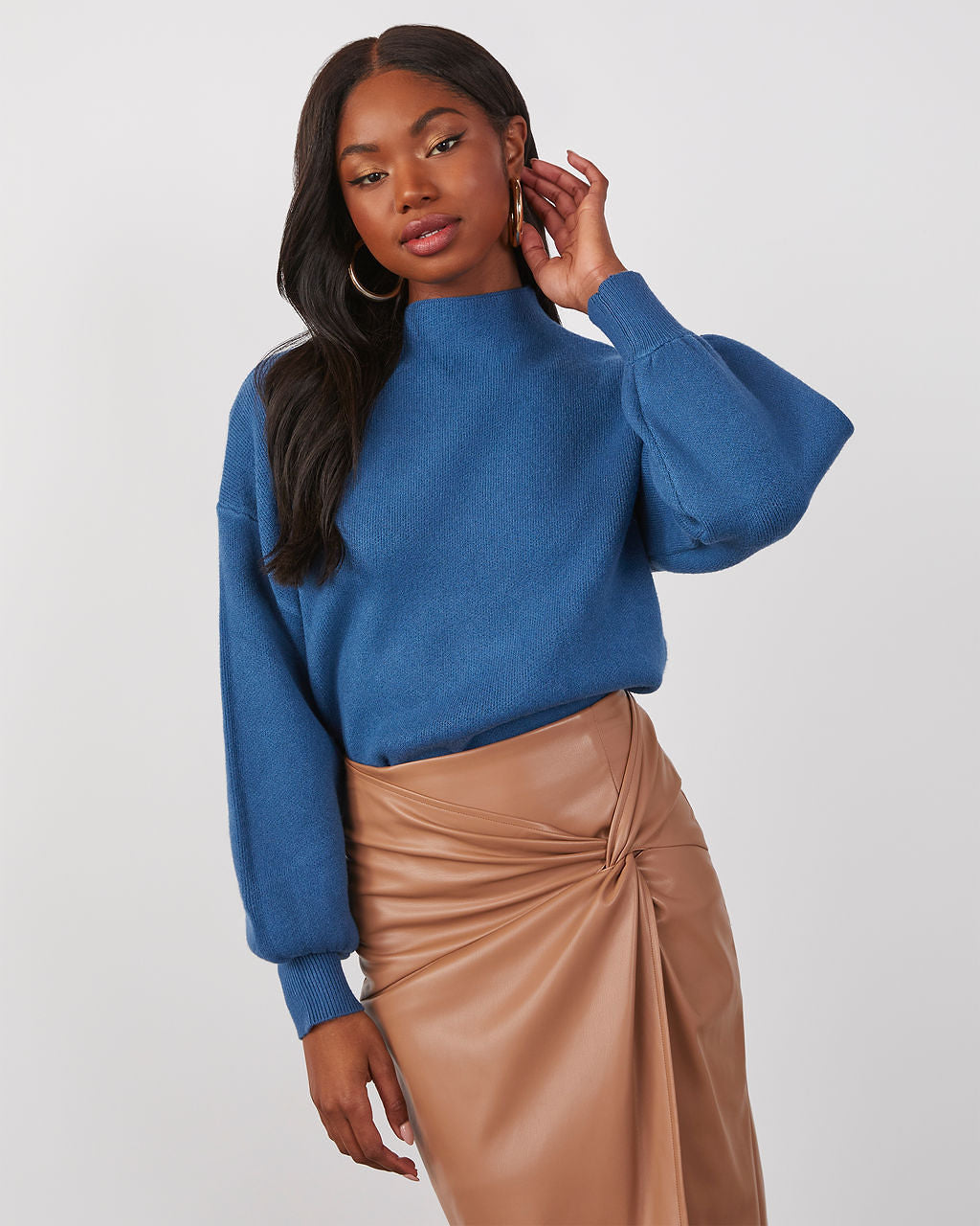 Blue mock neck knit sweater with long balloon sleeves and ribbed cuffs, paired with tan skirt.