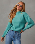 Mock neck sweater in teal, angled view with long sleeves and fitted ribbed cuffs