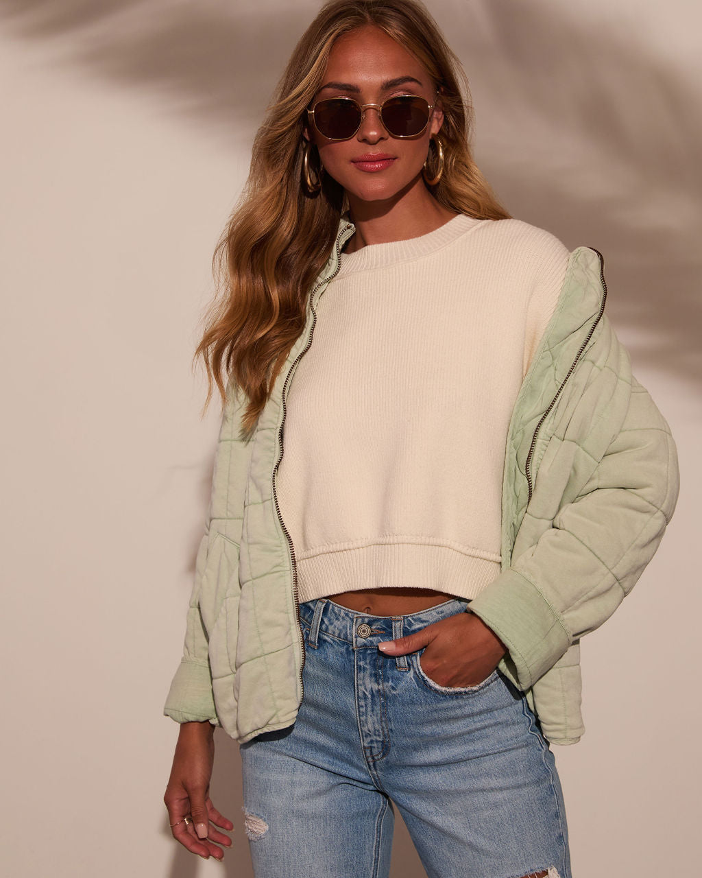 Quilted jacket in light green with zip front and stand collar over a knit top.