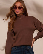 Mock neck sweater in dark brown, close view of neckline and long sleeves over jeans