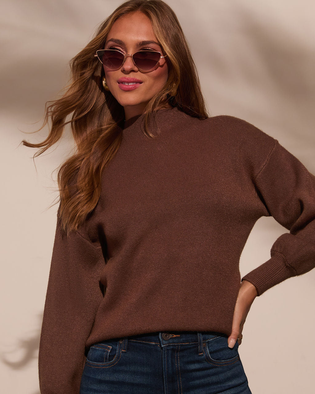 Mock neck sweater in dark brown, close view of neckline and long sleeves over jeans