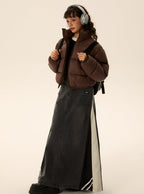 Brown short puffer jacket with zip front and stand collar, styled over denim-look long skirt