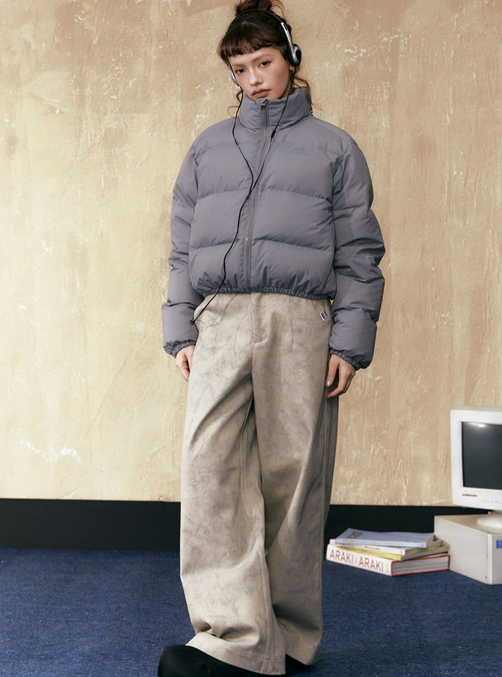 Gray short puffer jacket with full zip and stand collar, worn with wide-leg beige pants