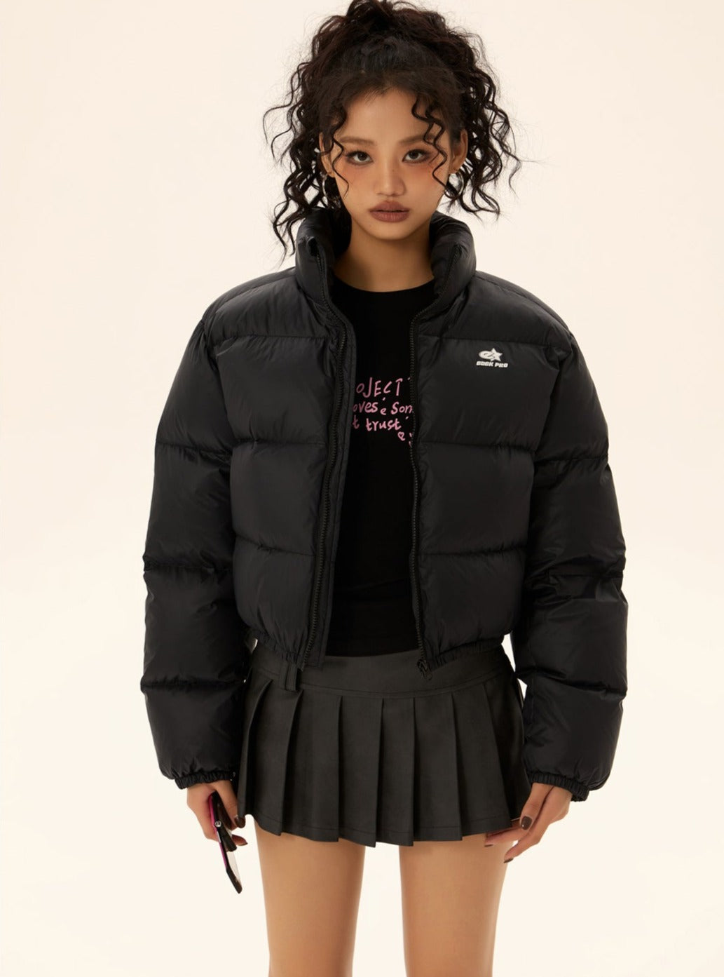 Black short puffer jacket with zip front and stand collar, paired with pleated skirt