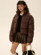 Brown short puffer jacket with zip front, side welt pockets, and pleated skirt hem