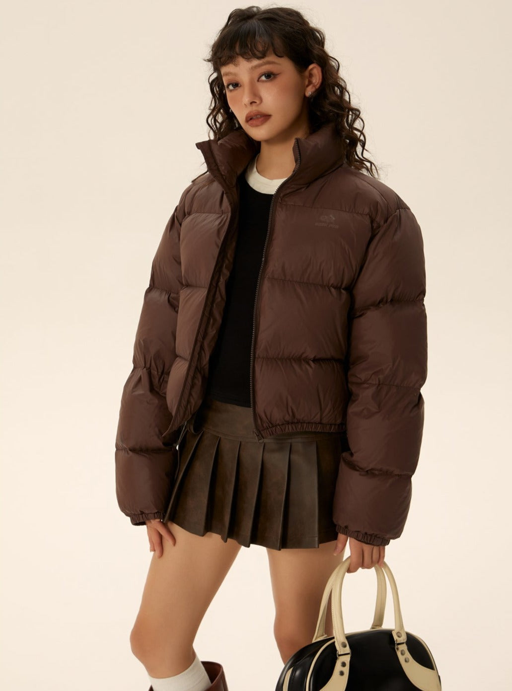 Brown short puffer jacket with zip front, side welt pockets, and pleated skirt hem
