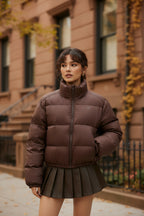 Brown short puffer jacket with zip front and elastic hem, paired with pleated skirt layer