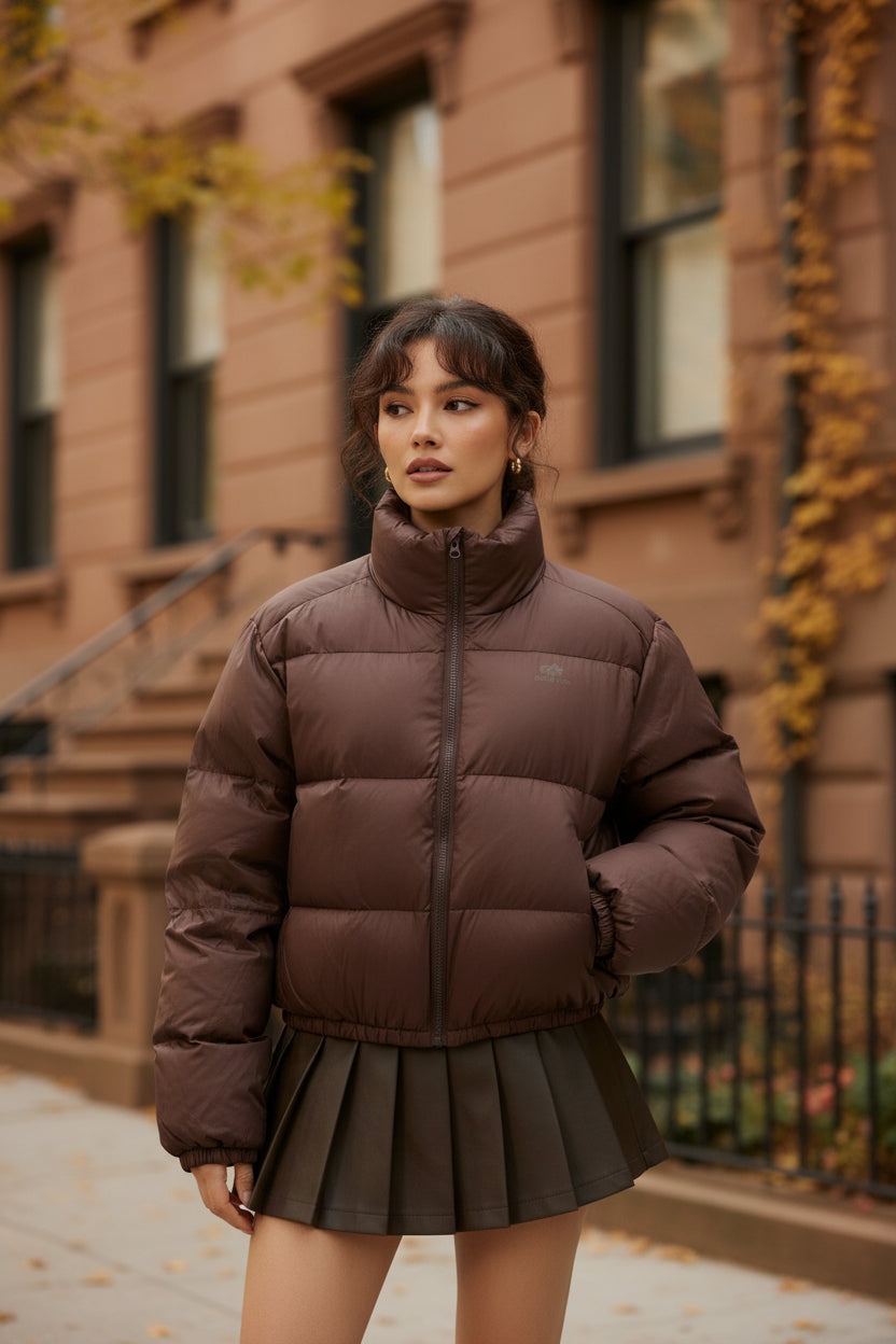 Brown short puffer jacket with zip front and elastic hem, paired with pleated skirt layer