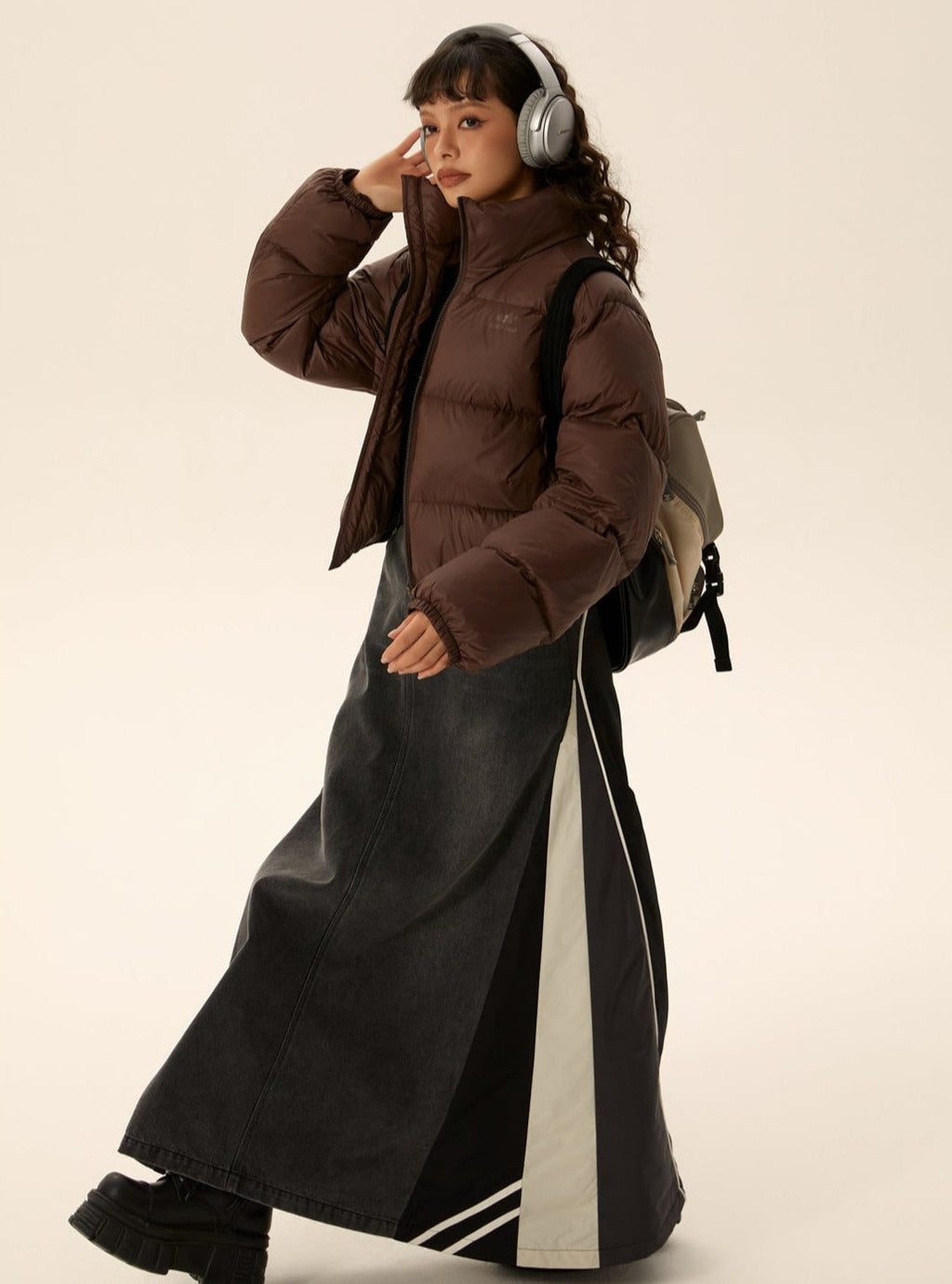 Brown short puffer jacket with zip front and stand collar, worn with long dark skirt