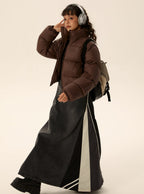 Brown short puffer jacket with zip front and stand collar, worn with long dark skirt