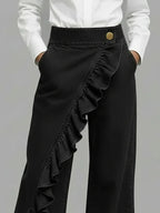 Black wide-leg jeans with diagonal ruffle overlay and gold button waistband