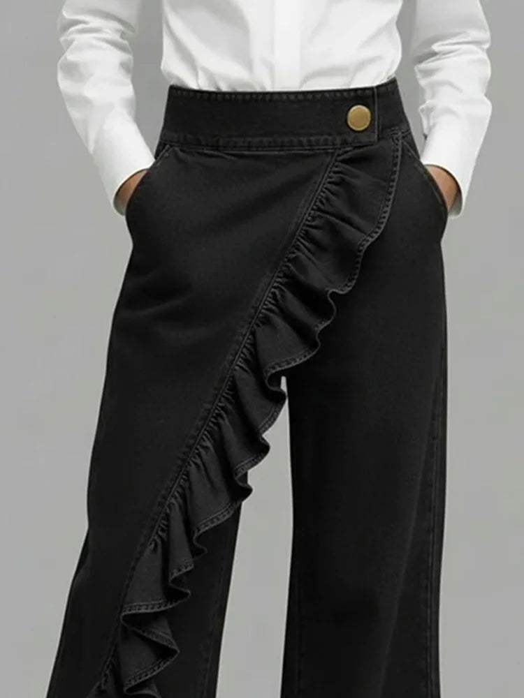 Black wide-leg jeans with diagonal ruffle overlay and gold button waistband