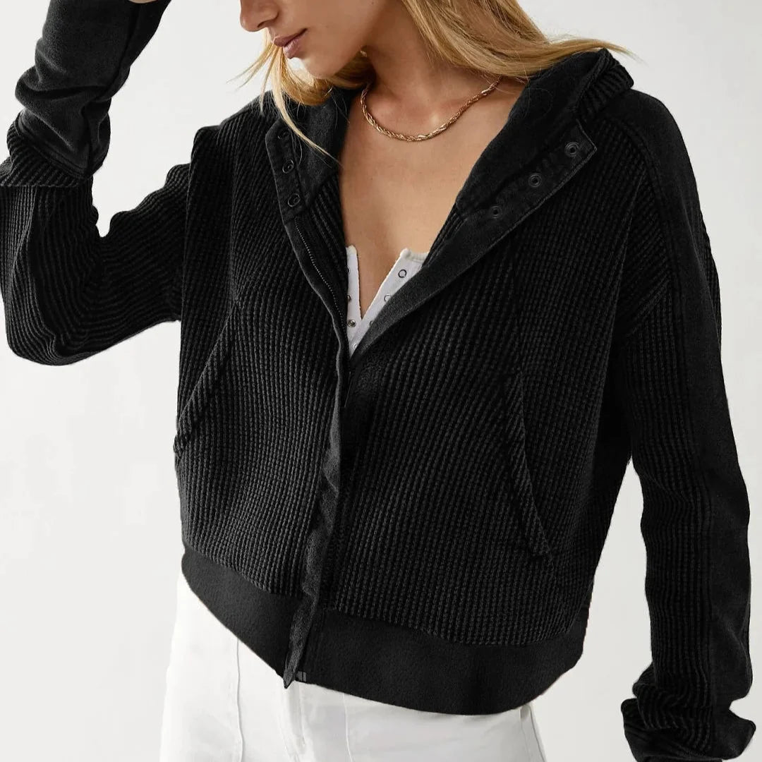 Close-up: black waffle knit zip hoodie with hood, snap buttons, and textured fabric.