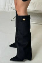 Black suede tall heeled boots with gold buckle on the top cuff, side view.