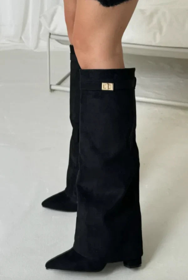 Black suede tall heeled boots with gold buckle on the top cuff, side view.