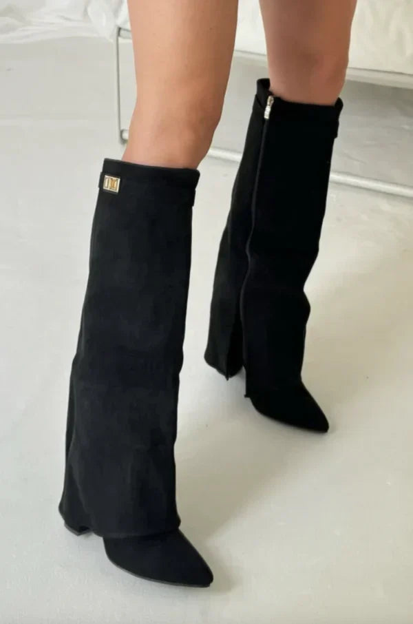 Black suede tall heeled boots with gold buckle on cuff; front view.
