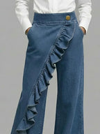 Blue wide-leg jeans with diagonal ruffle overlay and gold button waistband