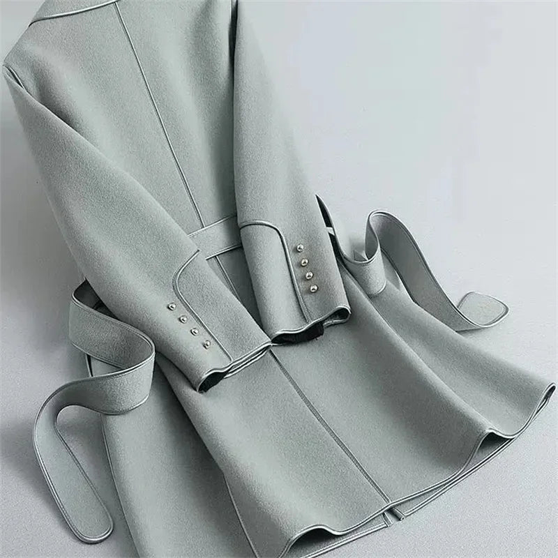 Light gray overcoat with vertical seam, belt at waist, and studded cuff