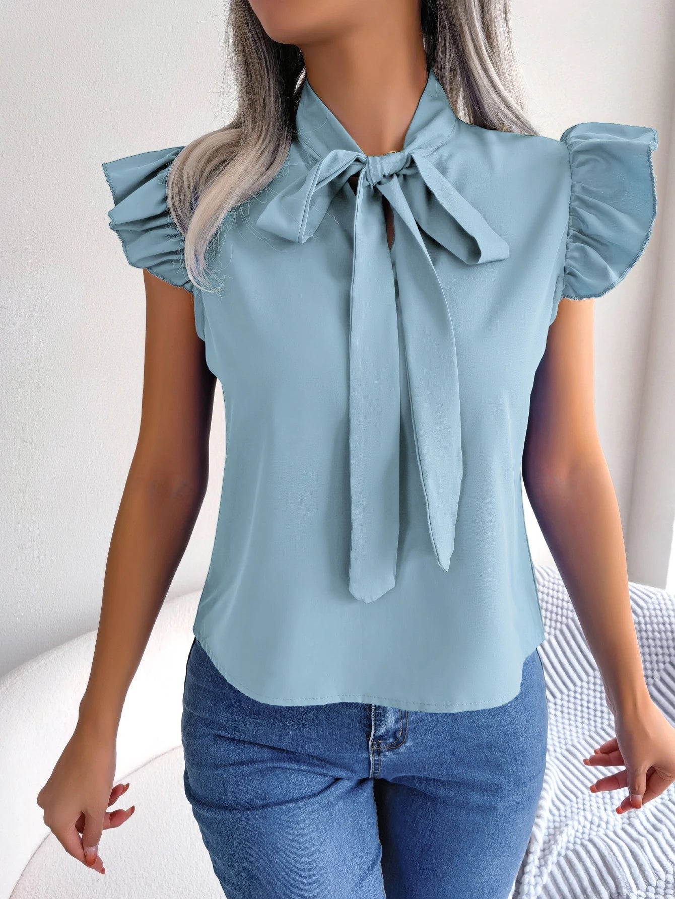 Light blue sleeveless blouse with bow tie neckline and ruffled shoulder accents