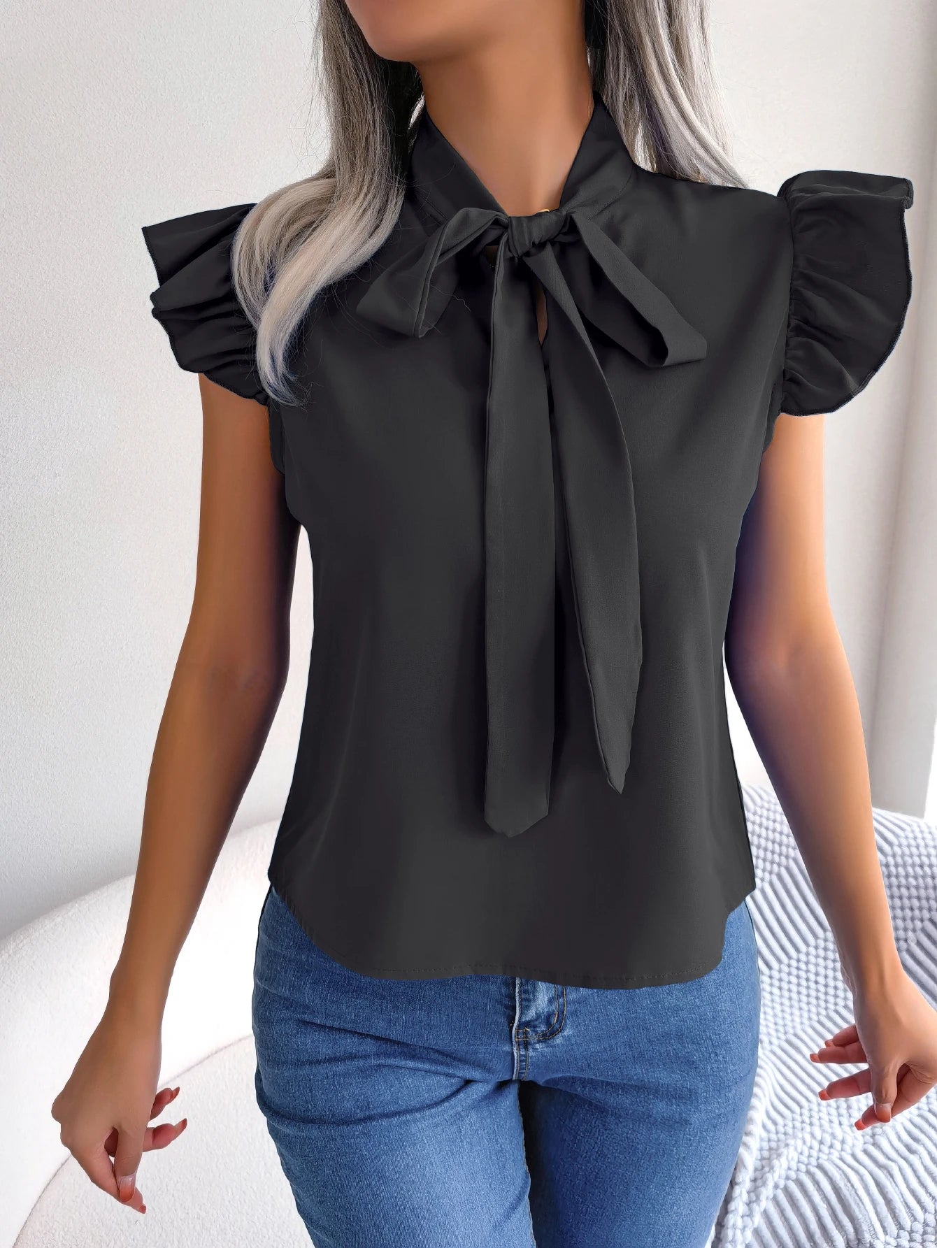 Black sleeveless blouse with bow tie neckline and ruffled shoulder detailing