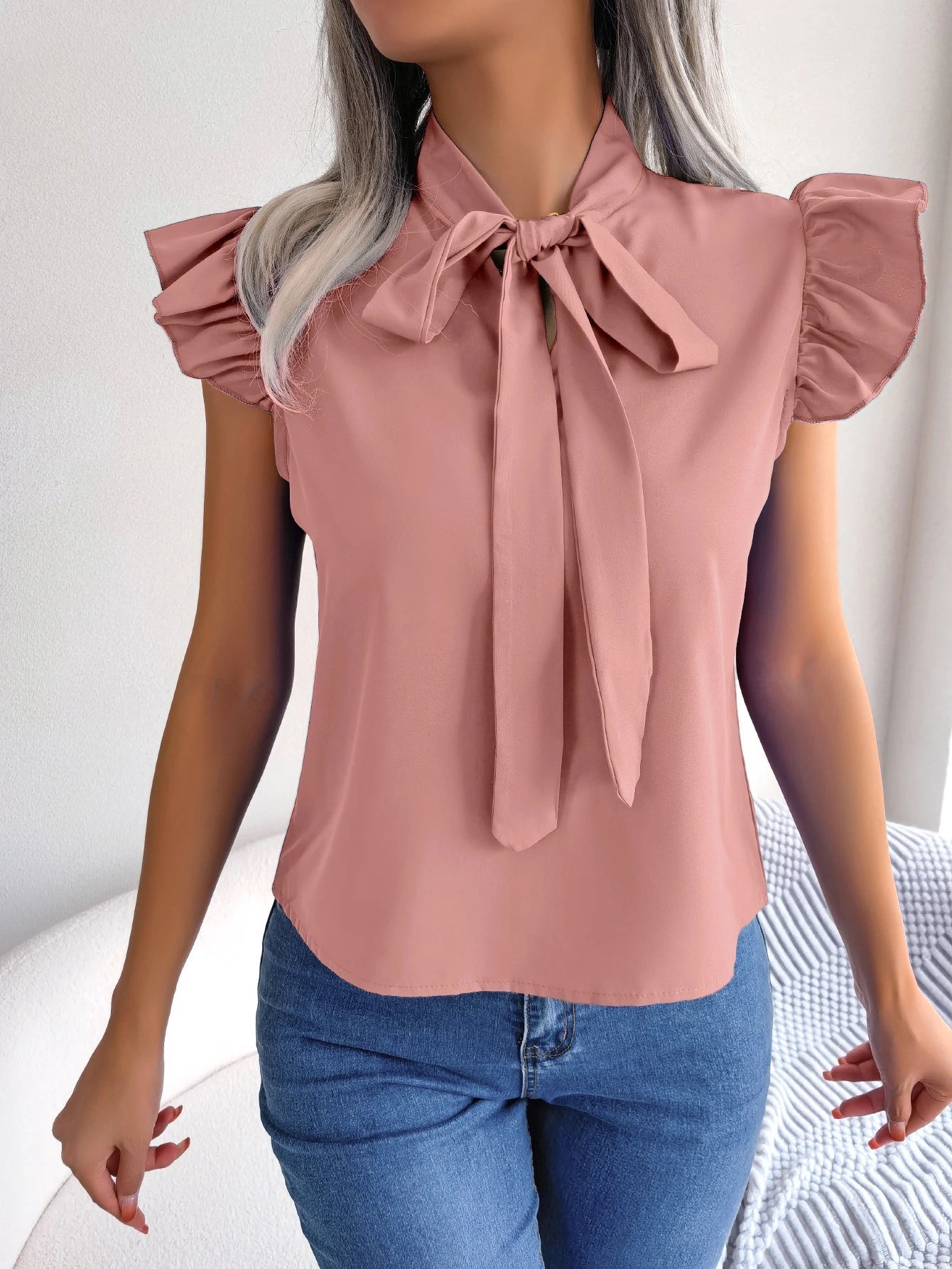Blush pink sleeveless blouse with bow tie neckline and ruffled sleeve shoulders